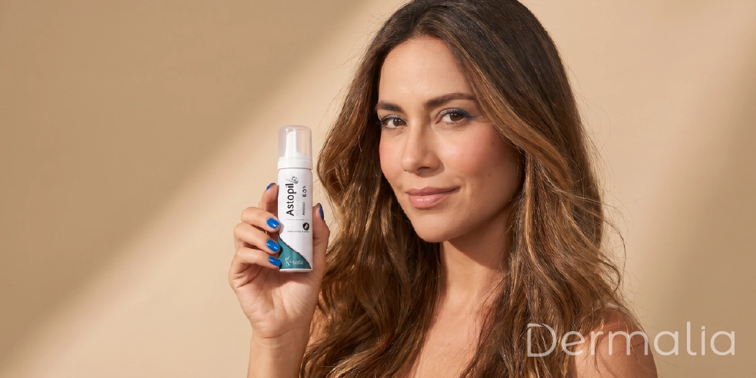 Cómo evitar la caída del cabello y fortalecer el cuero cabelludo. Mujer sosteniendo un tratamiento capilar tópico mientras muestra su cabello largo y saludable.