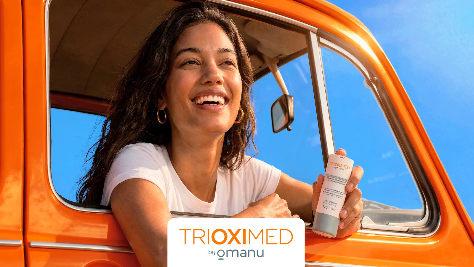 Mujer sonriendo desde una camioneta naranja sosteniendo crema despigmentante Trioximed durante un viaje de verano bajo el sol.