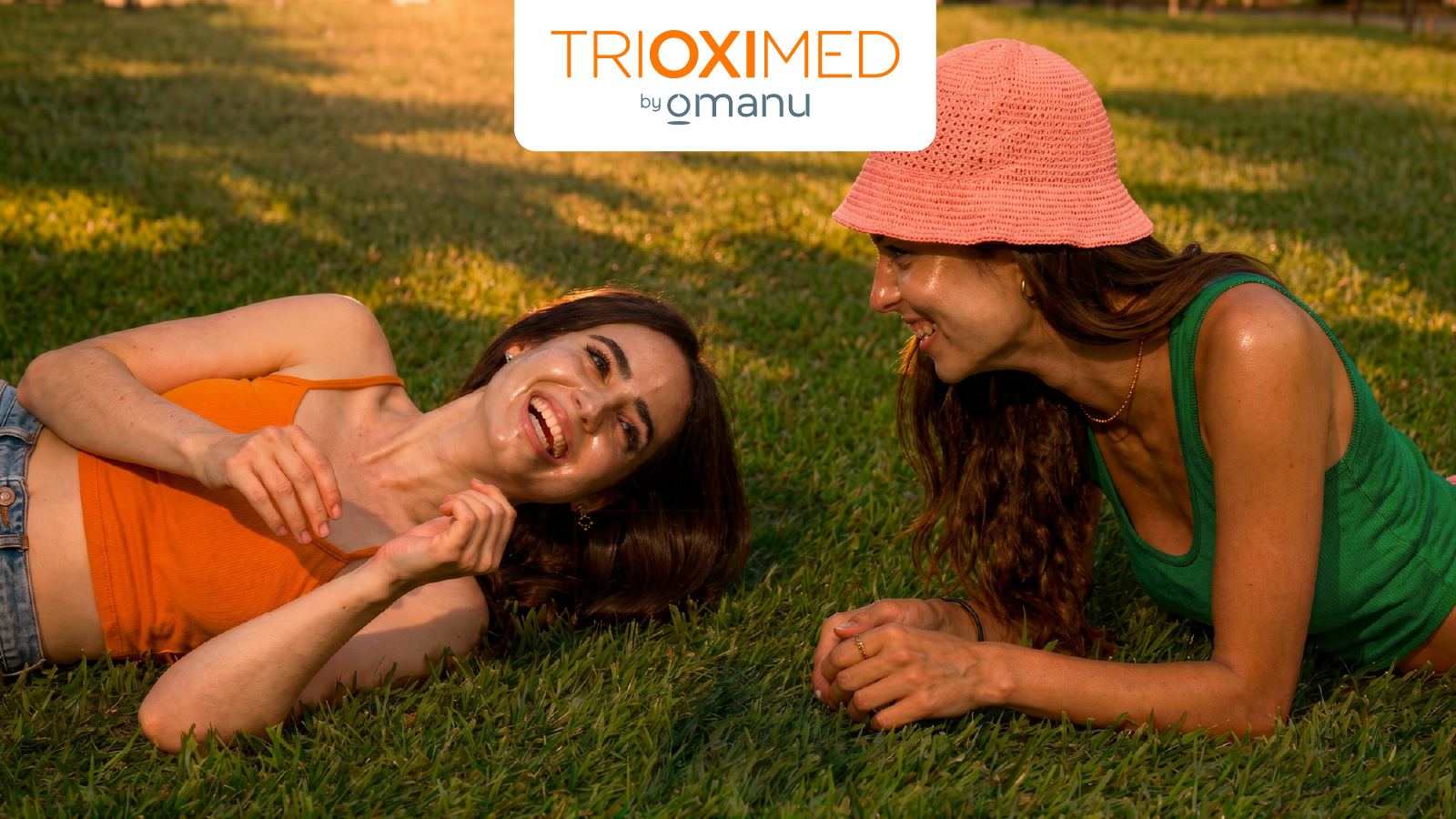 Dos mujeres disfrutando una tarde al aire libre sobre el césped, reflejando bienestar, confianza y cuidado de la piel en un estilo de vida saludable.
