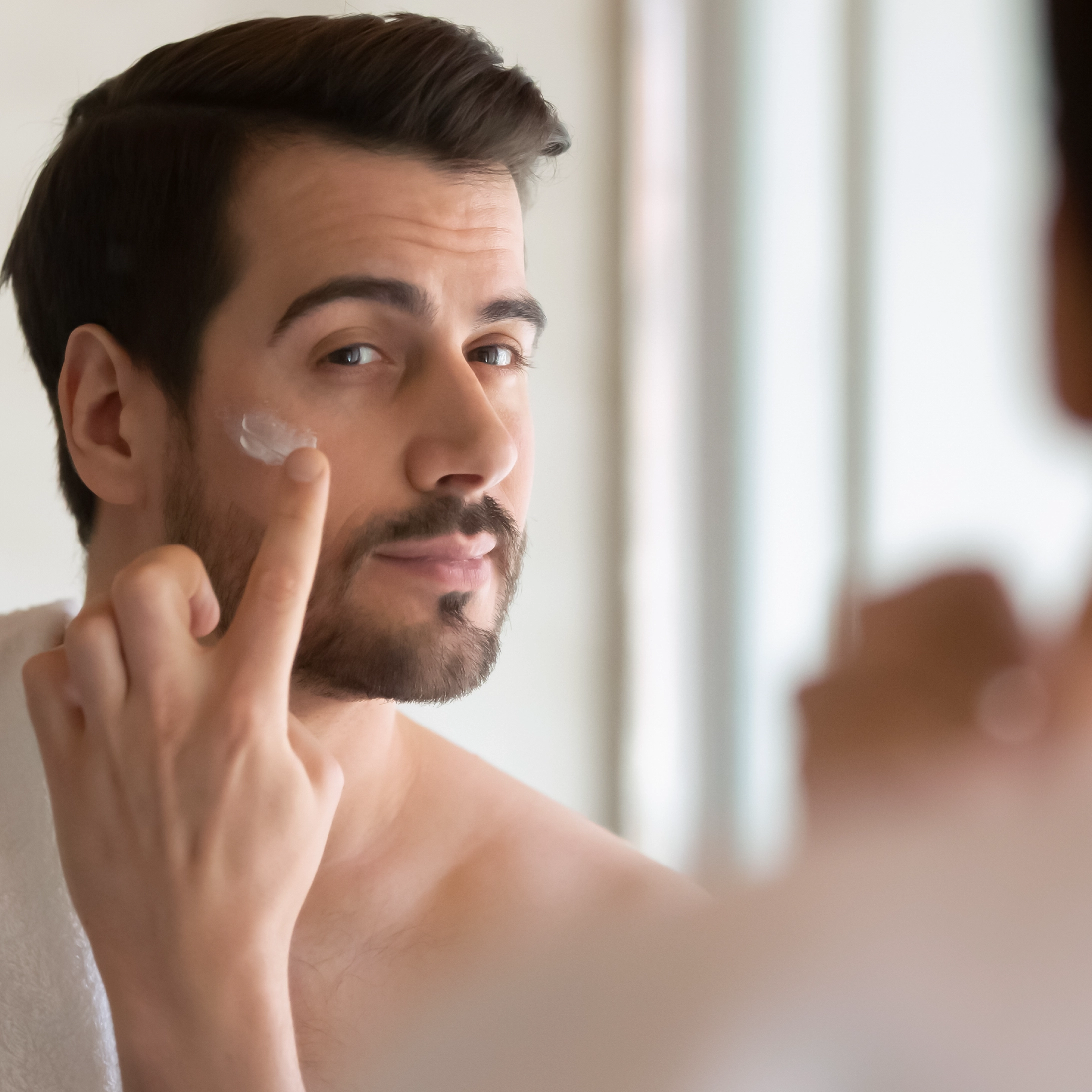 Hombre aplicando crema facial frente al espejo durante su rutina de skincare para hidratar y proteger la piel.
